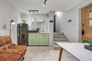 A compact kitchen with a refrigerator, stove, and green cabinets. There is a dining area with a table and a brown sofa. - Gaira House in Provenza by Nowa (Medellín)