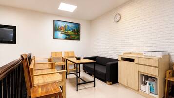 A furnished living room with a wooden dining set, a black sofa, and a white brick wall.
