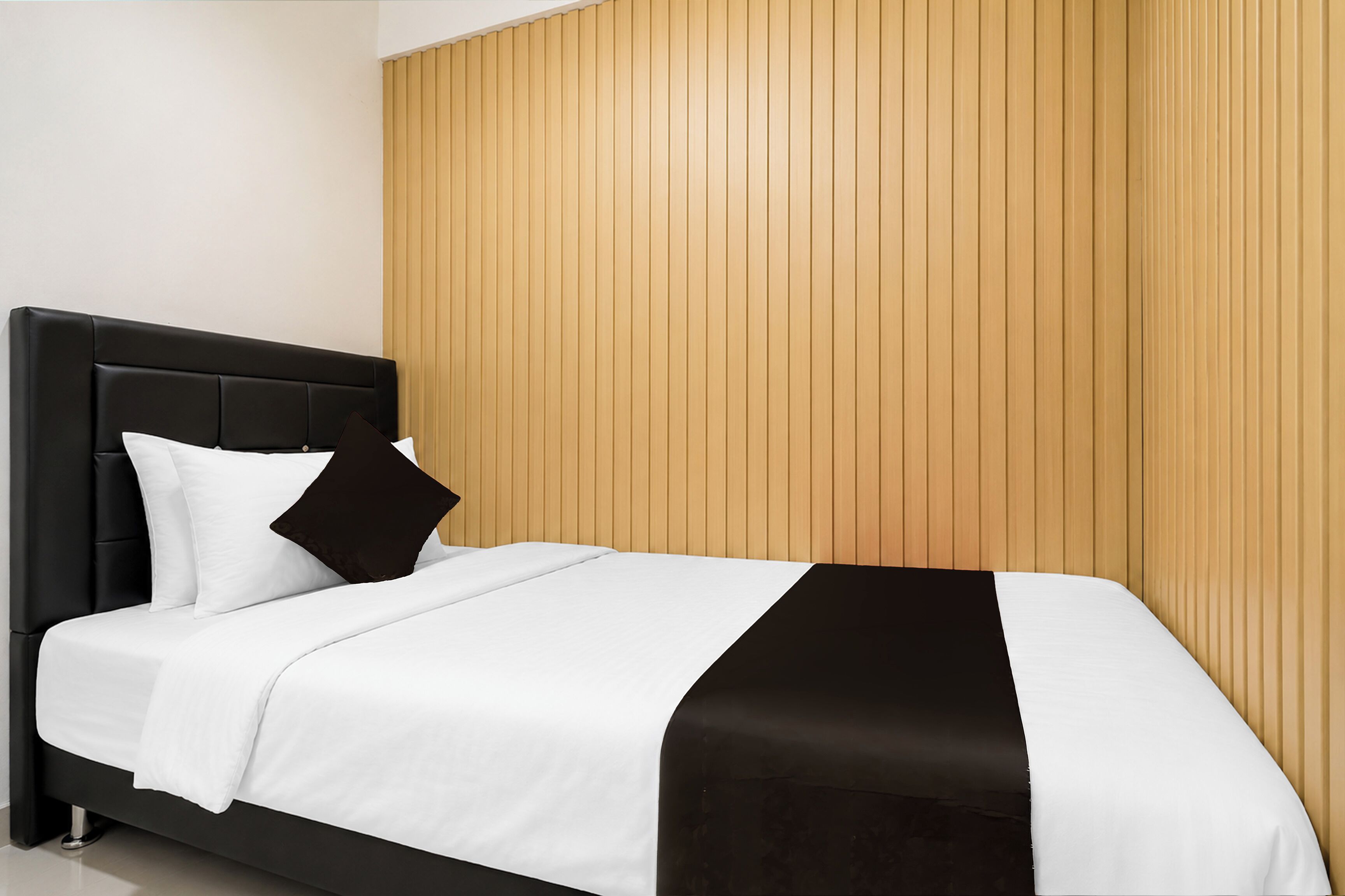 A modern bedroom with a black headboard, white bedding, and a wooden panel wall.