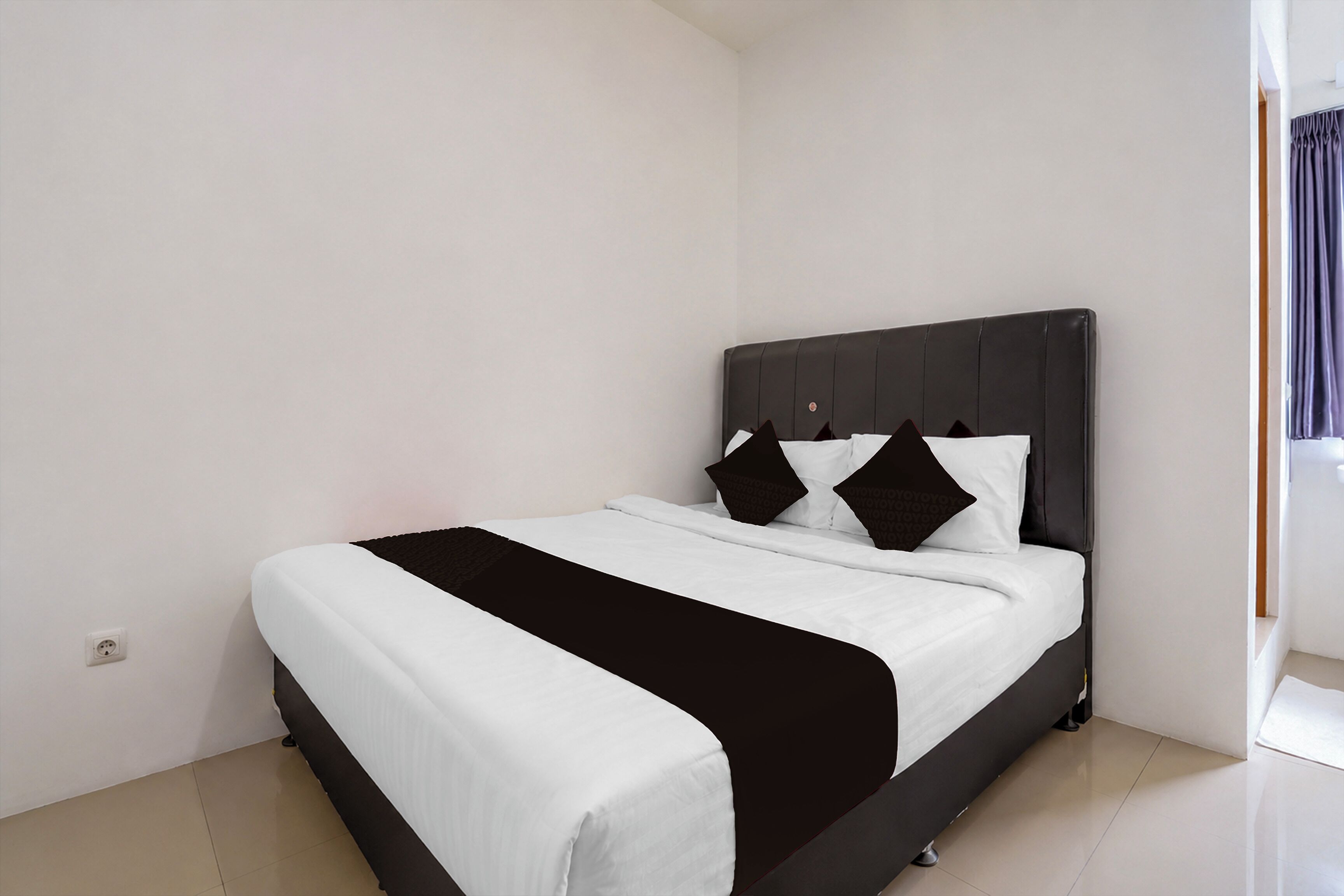 A single bed with a black headboard and white bedding in a room with plain walls and a tiled floor.
