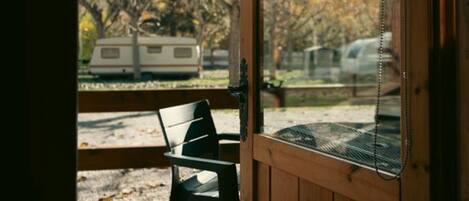 Une terrasse en bois avec un banc, une fenêtre donnant sur les arbres et un camping-car.