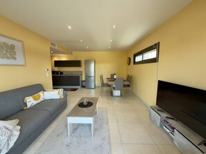 A compact living space with a sofa, a coffee table, a TV, a kitchen area, and a dining table. - Bright apartment with AC - 4 guests (Argelès-sur-Mer)