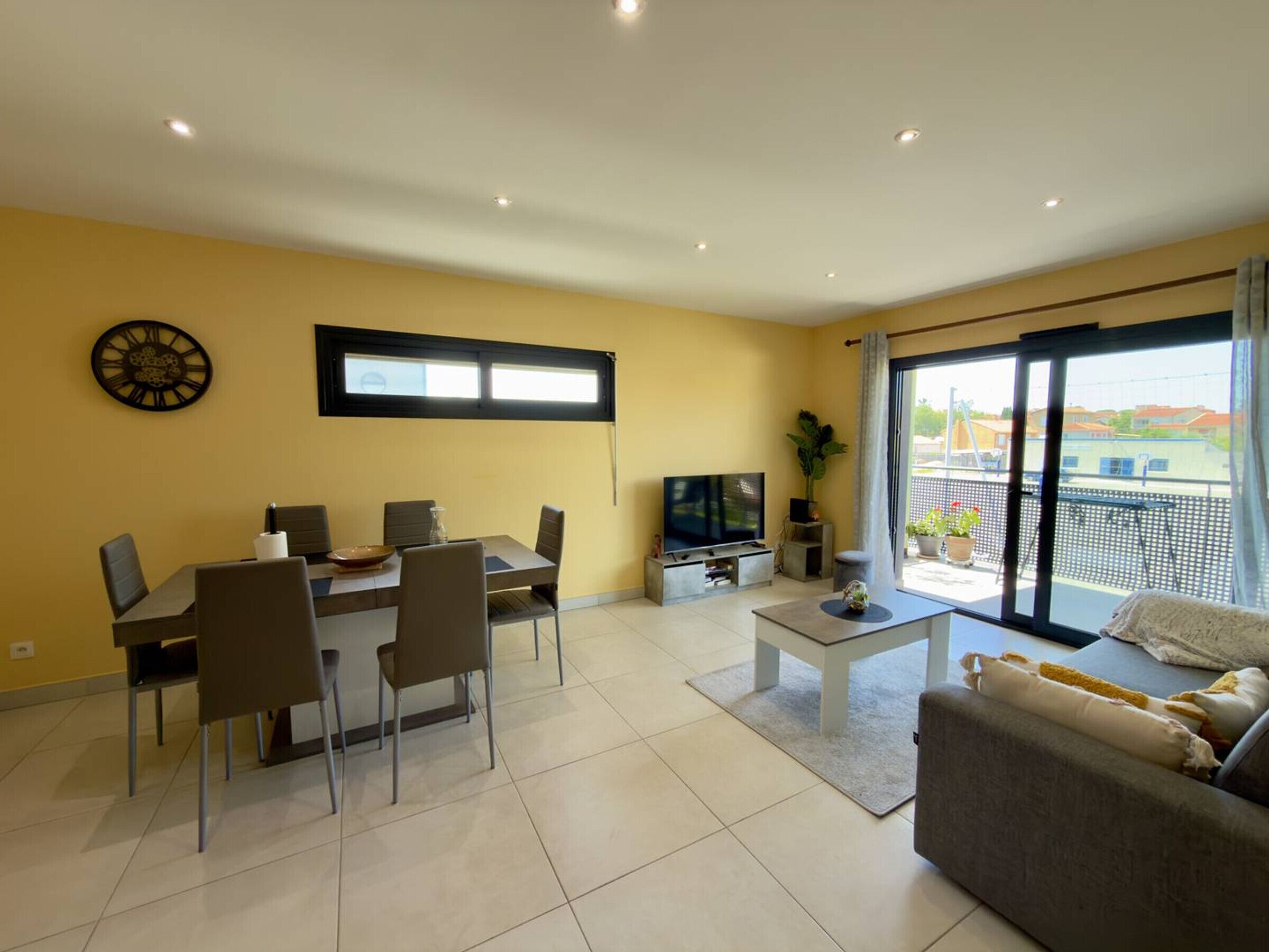 A living room with a dining area, a television, and a balcony with a view.