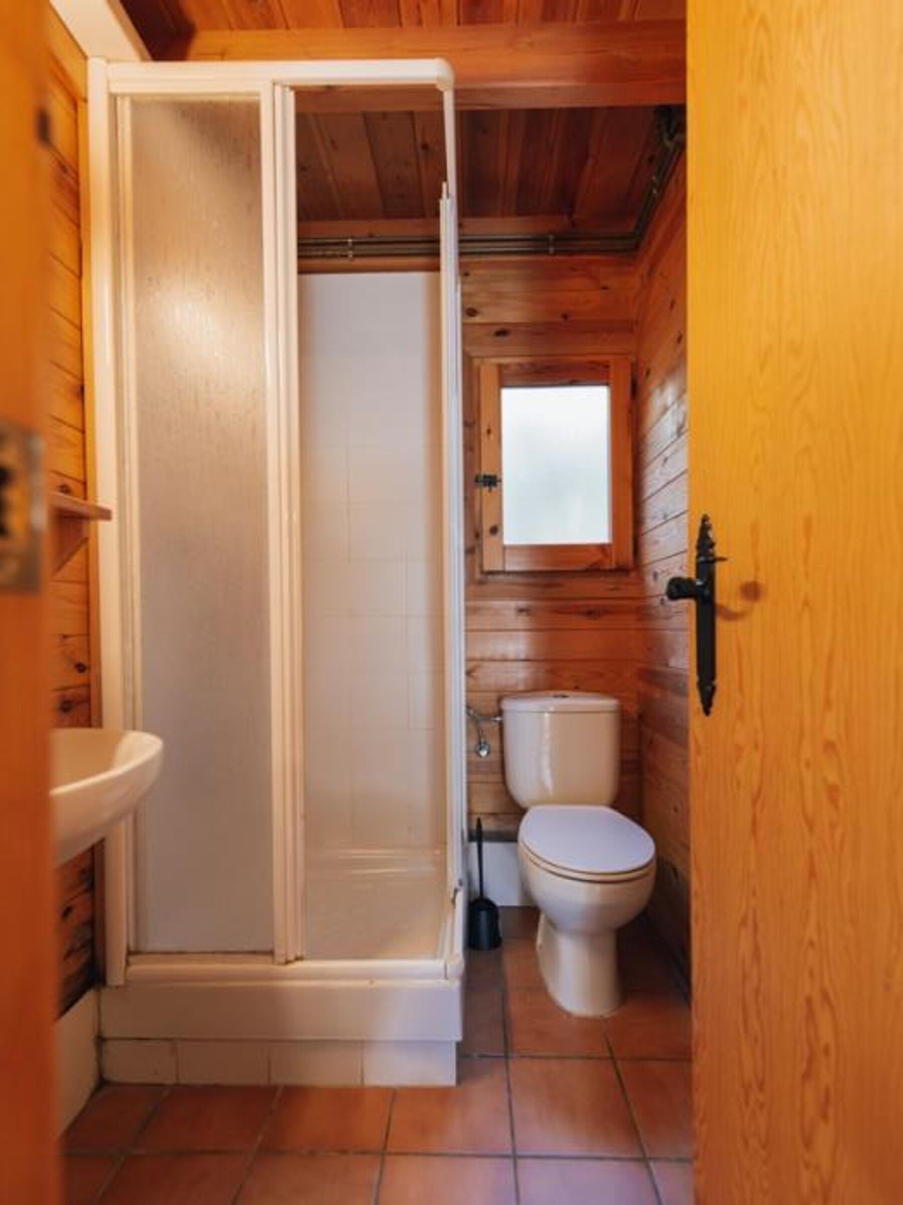 A wooden cabin bathroom with a shower, toilet, and sink.