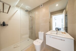 A modern bathroom with a glass shower enclosure, a white toilet, and a vanity with a mirror. - GuestReady - Carolina Building: Ground Floor Right (Lisbon)