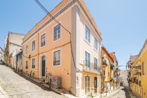 A narrow street with buildings on both sides, featuring balconies and a cobblestone path. - GuestReady - Carolina Building: Ground Floor Right (Lisbon)