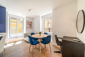 Ein modernes Wohnzimmer mit einem runden Holztisch, blauen Stühlen, einer Couch und einem großen Fenster mit Blick auf Gebäude.