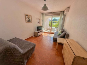Ein Zimmer mit einer Couch, einem Fernseher, einem Holztisch und einem Balkon mit Blick.