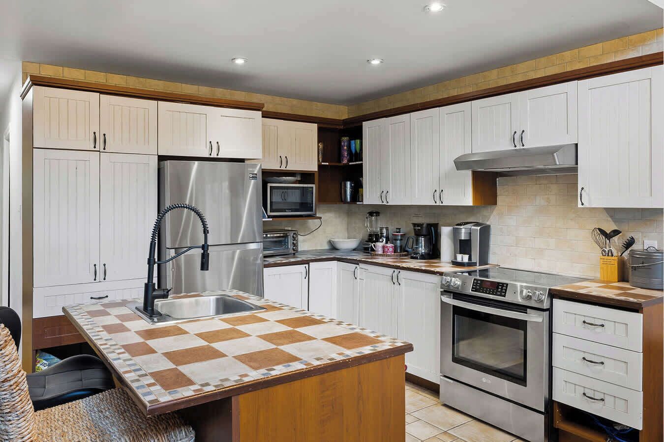 A modern kitchen with white cabinets, stainless steel appliances, a checkered island, and a built-in oven.