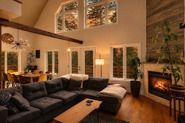 A spacious living room with a large sectional sofa, a fireplace, and a dining area with natural light from large windows.