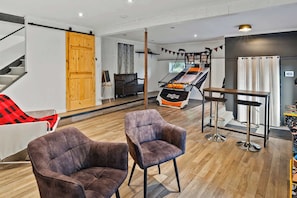 Un salon moderne avec un escalier, un panier de basketball et deux fauteuils.