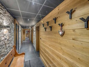 Un couloir aux murs en bois, agrémenté de quelques éléments en pierre et muni d’un banc.