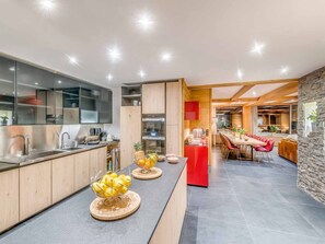 A modern kitchen with a central island, a dining area with red chairs, and a stone accent wall. - Spacious apartment, panoramic view - 14 guests (Tignes)