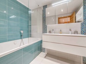 Une salle de bain moderne avec une douche à parois de verre, un meuble-lavabo blanc avec un miroir et un mur recouvert de carreaux.
