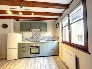 Eine Küche mit Holzbalken, einem Einbauofen, einem Kühlschrank und einem Fenster mit Jalousien.