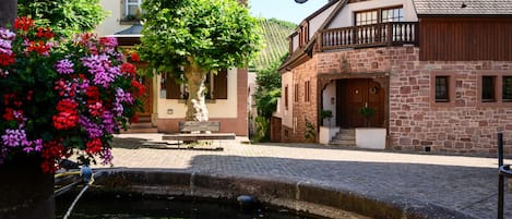 A courtyard with a stone fountain, a bench, and a tree with flowers.