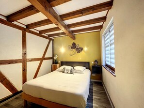 Ein Schlafzimmer mit einem Bett, Holzbalken, einer Wandleuchte, einer Buddha-Statue und einem Fenster mit Jalousien.