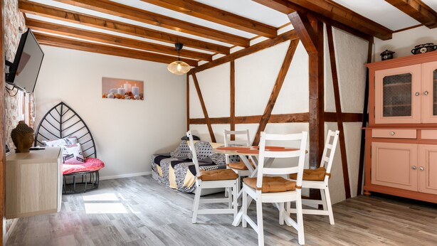 A room with a wooden ceiling, a dining table with chairs, a sofa, and a cabinet.