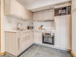 Eine kompakte Küche mit heller Holzvertäfelung, einer eingebauten Mikrowelle, einem Toaster und einem Edelstahlbackofen.