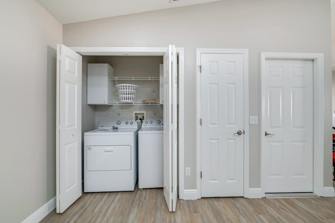 A laundry room with two stacked washers and dryers, a basket, and a shelf.