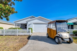 A white single-story house with a garage, a white picket fence, and a vehicle parked in front.