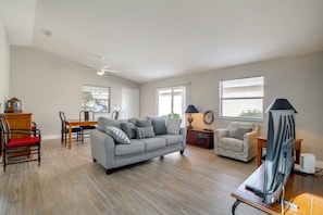 A spacious living room with a grey sofa, a wooden dining table, and a television.