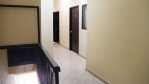 A hallway with a black railing, beige walls, and tiled flooring.