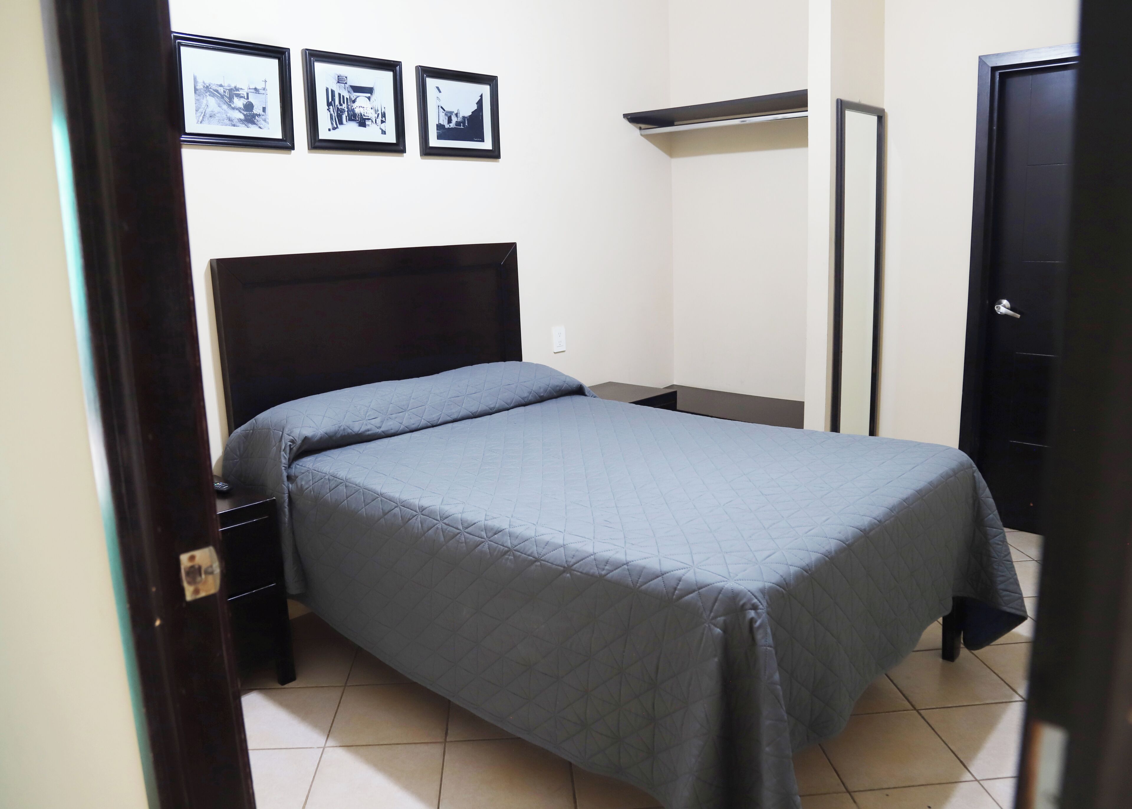 A bedroom with a bed, a nightstand, a dresser, and three framed pictures on the wall.