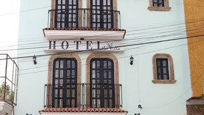 A hotel with a light facade, a balcony with black railings, and a sign reading 'HOTEL Villa.'