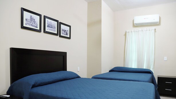 A bedroom with two beds, a black headboard, and three framed pictures on the wall.