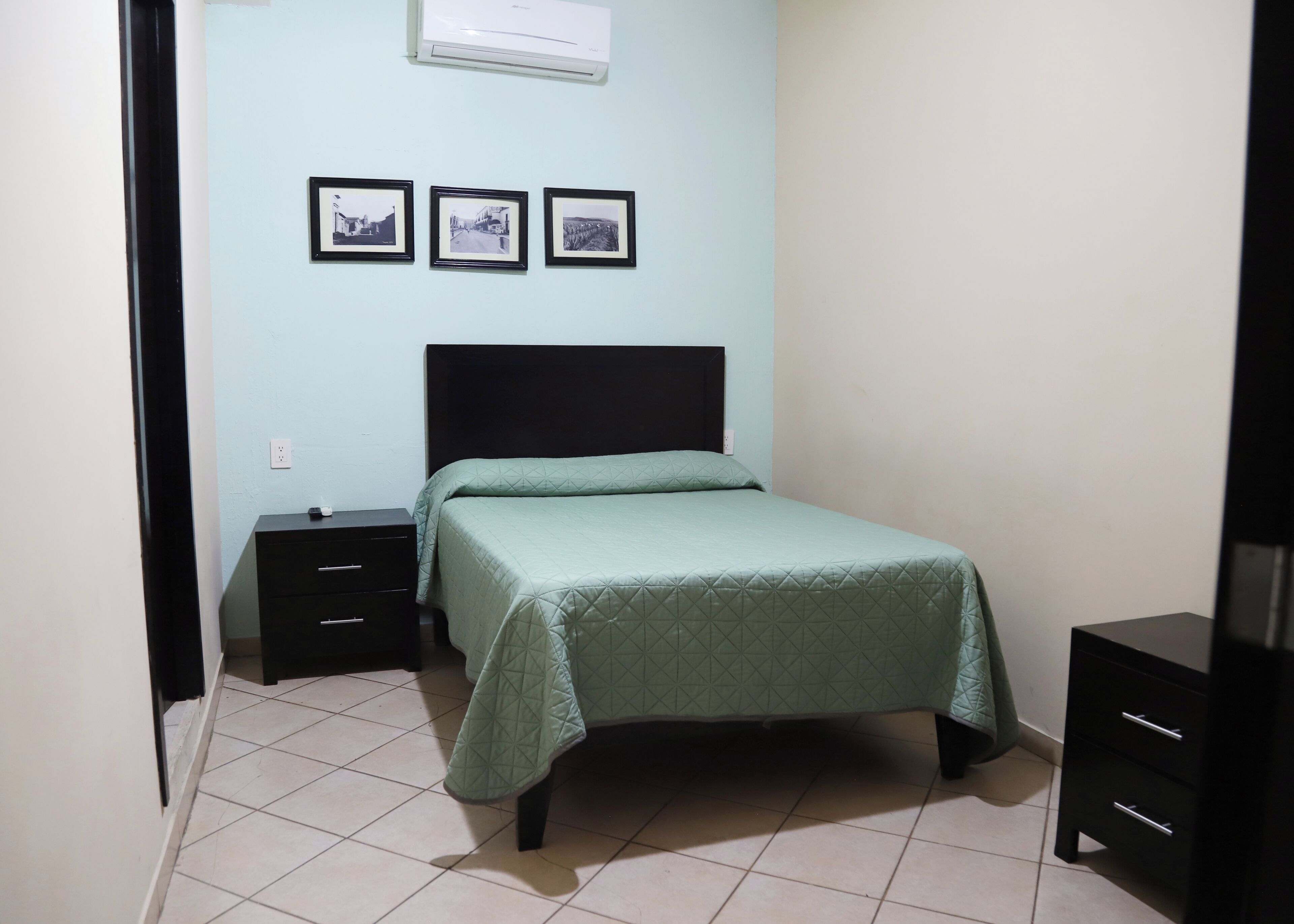 A bedroom with a bed, a nightstand, a dresser, and three framed pictures on the wall.