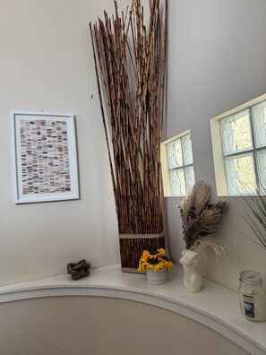 A room with a white wall, a framed abstract art piece, a tall decorative reed structure, a vase with yellow flowers, a candle, and a window with a view. - HTX hotspot: 3bd private & spacious townhome centrally located in Houston (Houston)