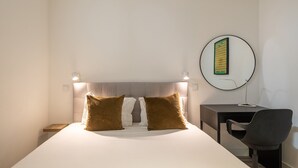 Una camera d'albergo con un letto, due cuscini, una scrivania, una sedia e uno specchio fissato alla parete.