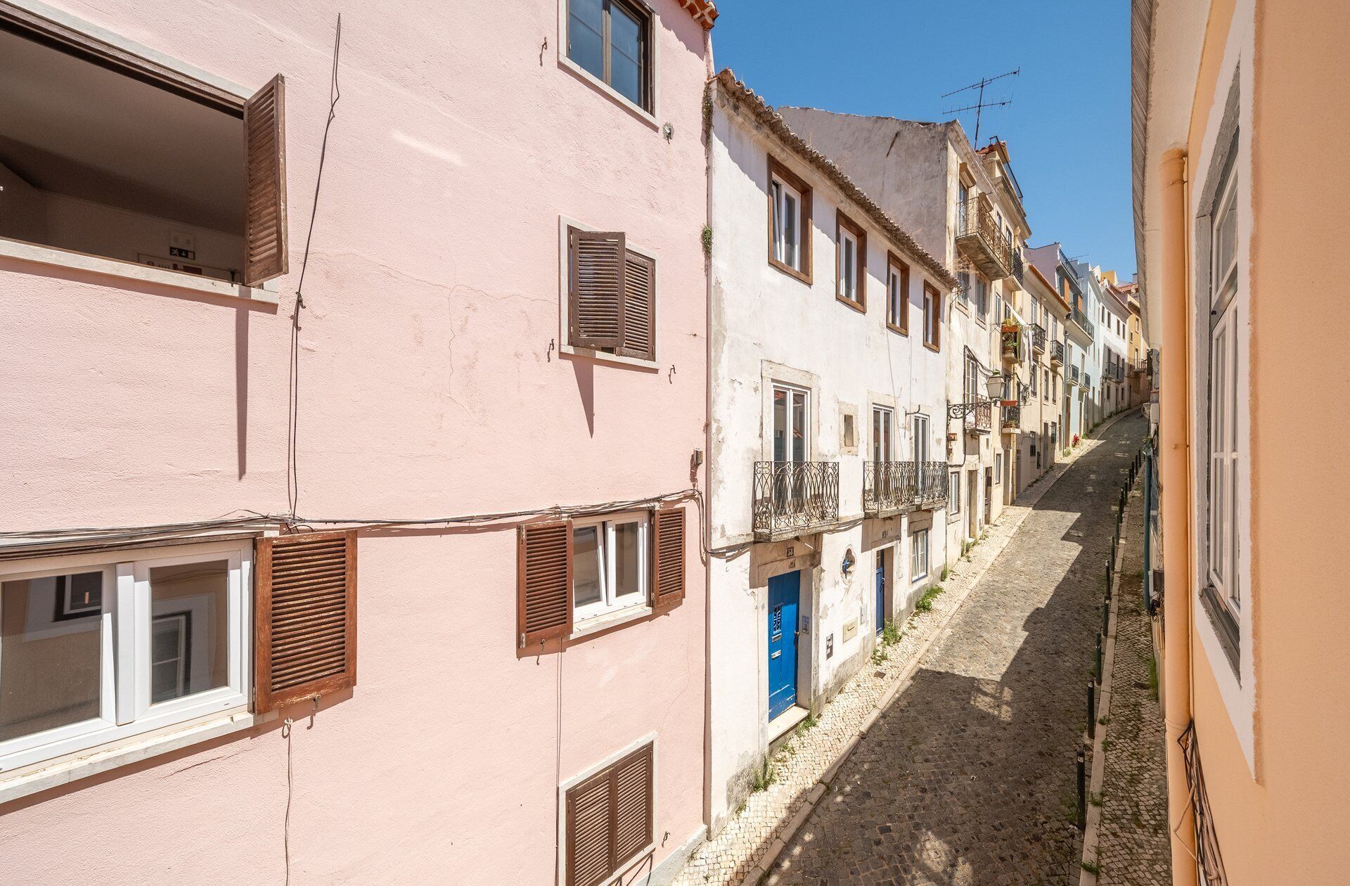 Une rue étroite bordée d’immeubles, dont certains sont dotés de balcons et de volets.