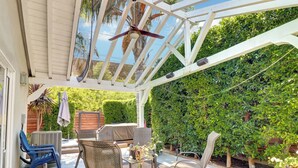 Eine überdachte Terrasse mit Gartenmöbeln, einem Deckenventilator und Blick auf einen üppigen Garten.