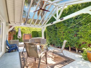 Eine überdachte Terrasse mit Gartenmöbeln, einem Deckenventilator und Blick auf einen üppigen Garten.