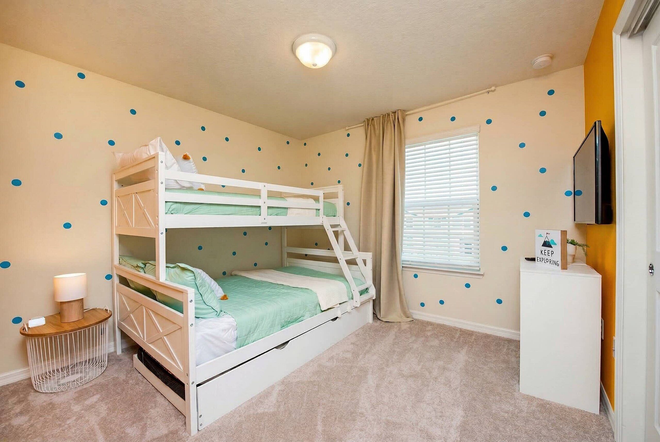 A bunk bed room with a desk, a lamp, and a wall with blue dots.