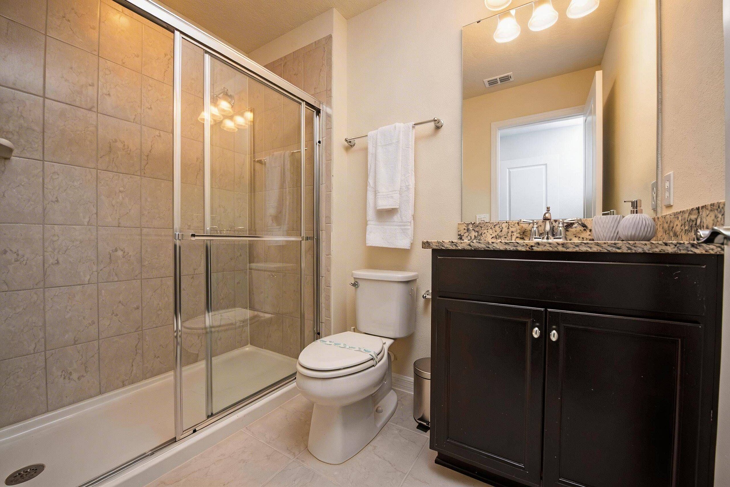 A bathroom with a glass-enclosed shower, a toilet, a sink with a marble countertop, and a dark wooden cabinet.