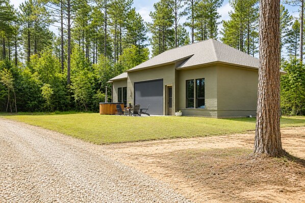 A single-story house with a garage, a patio with outdoor furniture, and a forested background.
