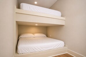 Ein Stockbett mit weißer Bettwäsche in einem Zimmer mit beigen Wänden und Holzboden.
