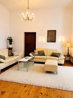Ein Wohnzimmer mit einer Chandelüster, einer Holztür, einer Sofagarnitur, einem Couchtisch und einer Lampe.