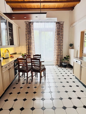 A kitchen with a dining table, chairs, and a window with curtains. - Villa on Lake Wangermeer—North Sea vacation, sun terrace, 4 guests, dog-friendly (Wangerland-Hohenkirchen)