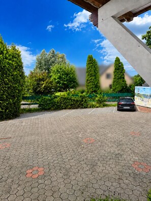 A paved parking area with a car, surrounded by well-maintained hedges and trees under a clear sky. - Villa on Lake Wangermeer—North Sea vacation, sun terrace, 4 guests, dog-friendly (Wangerland-Hohenkirchen)