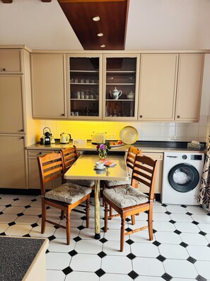 A kitchen with a dining table, chairs, a washing machine, and cabinets. - Villa on Lake Wangermeer—North Sea vacation, sun terrace, 4 guests, dog-friendly (Wangerland-Hohenkirchen)