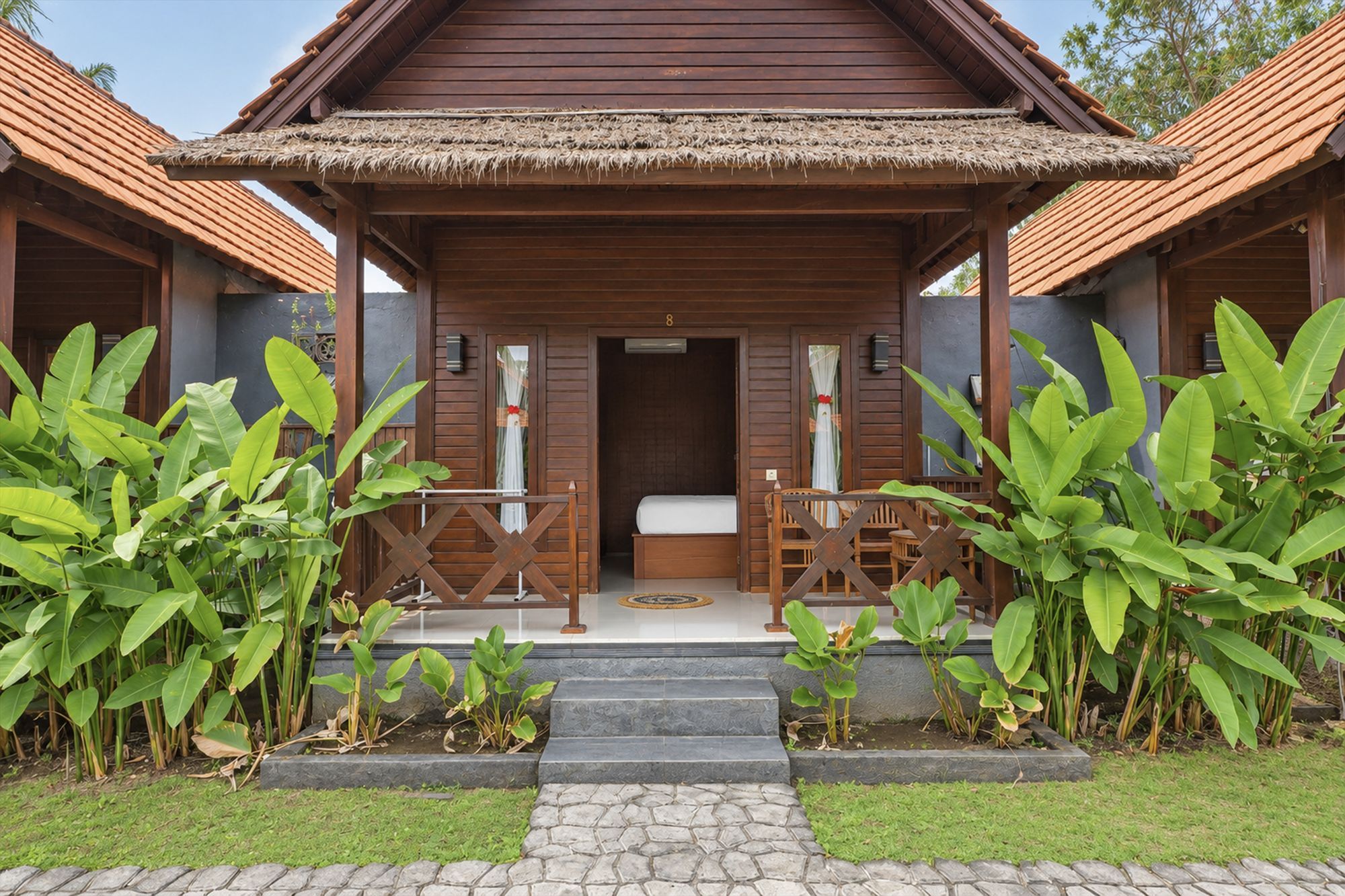 A wooden building with a thatched roof entrance, a bed, and a small table with chairs.