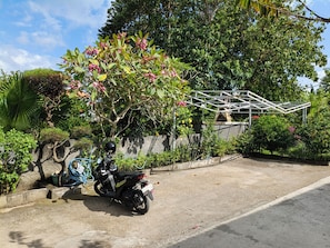 Una motocicleta estacionada en un jardín con una estructura de invernadero al fondo.