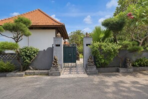 A gated entrance with a tiled roof, a pathway leading to a building, and various statues and plants. - Belvilla near Sampalan Beach formerly Ar (Penida Island)