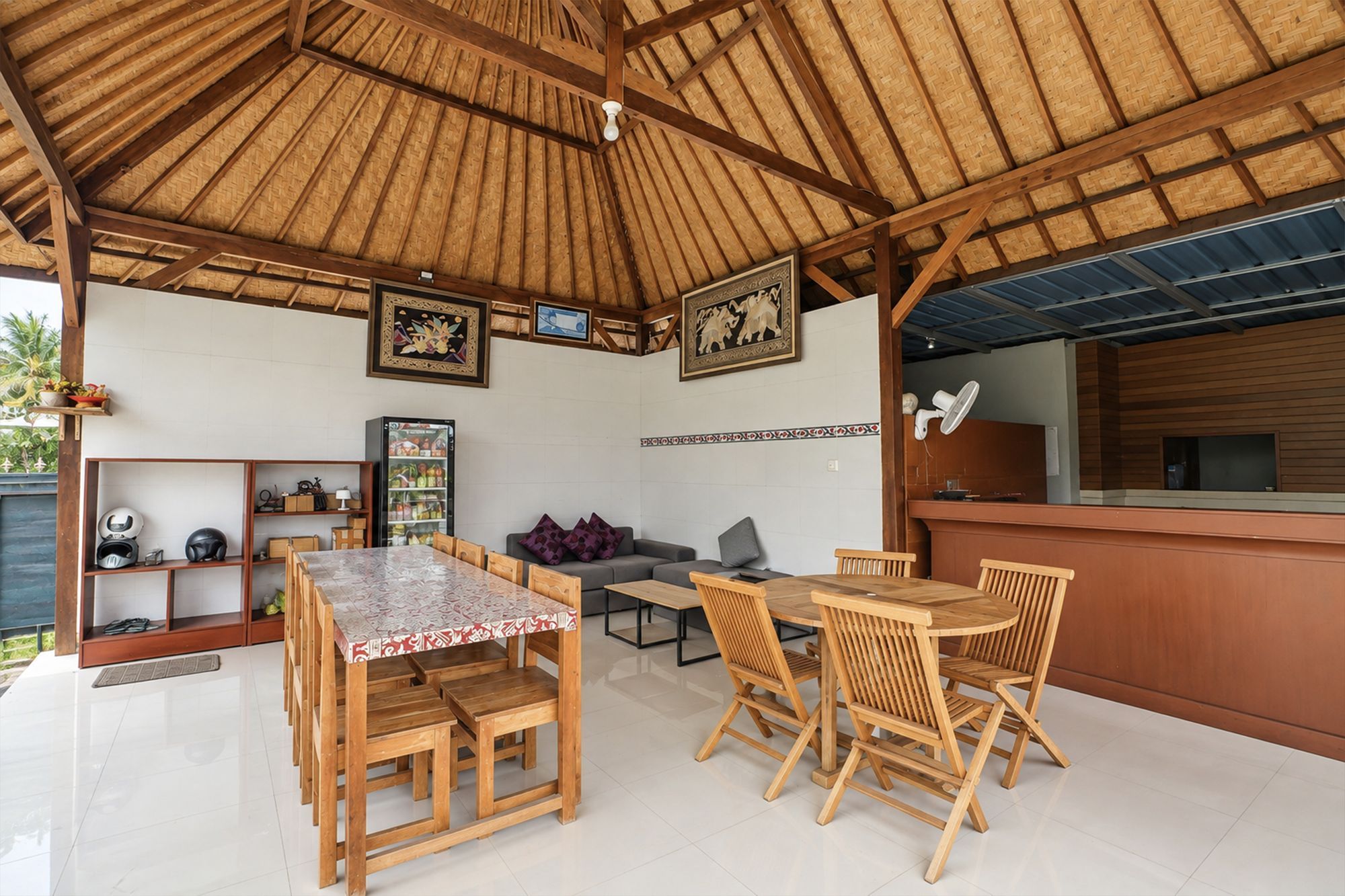 Un área de estar techada al aire libre con muebles de madera, un refrigerador y decoración en las paredes.