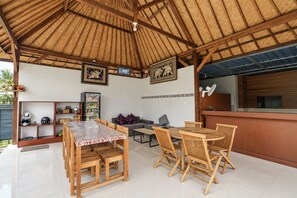 Un área de estar techada al aire libre con muebles de madera, un refrigerador y decoración en las paredes.