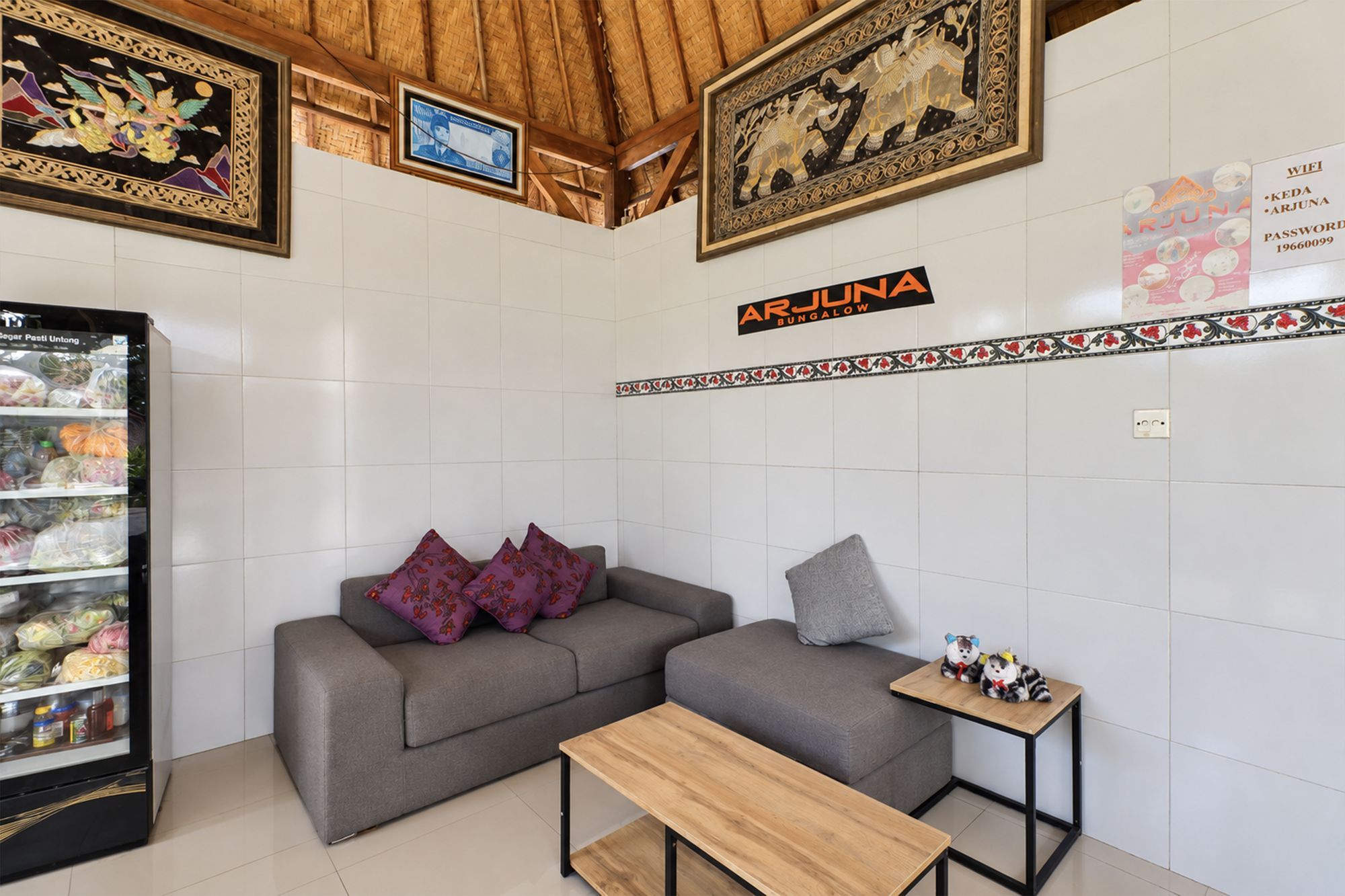 Una habitación con un sofá gris, una pequeña mesa de madera y un refrigerador lleno de comida.